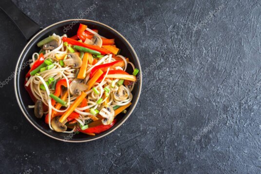Padella wok con verdure, noodles e condimenti asiatici.
